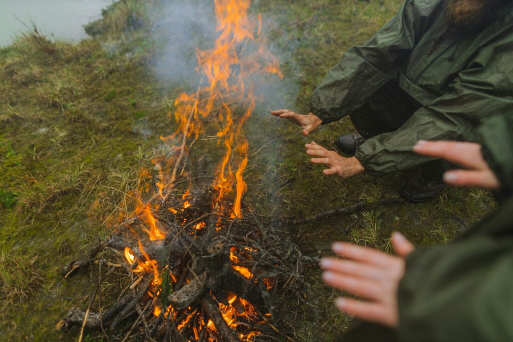 People warming their hands by a campfire in a serene outdoor setting.