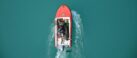 Top view of a red motorboat with fishermen navigating open turquoise waters.