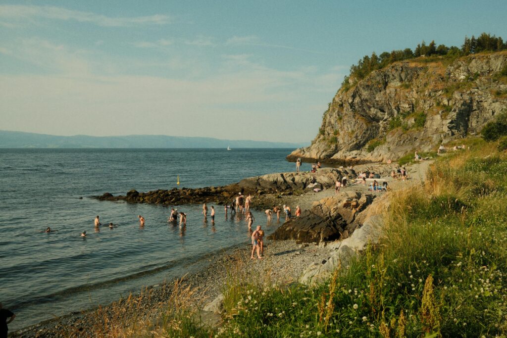 People enjoying a sunny day at a rocky beach with a scenic cliff.