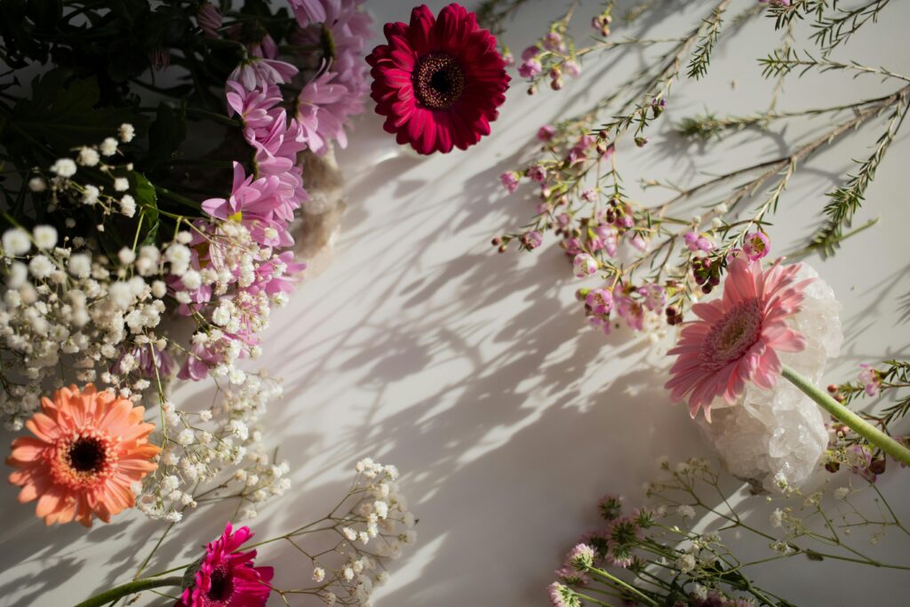 A colorful flat lay of various flowers on a white surface with sunlight casting shadows.